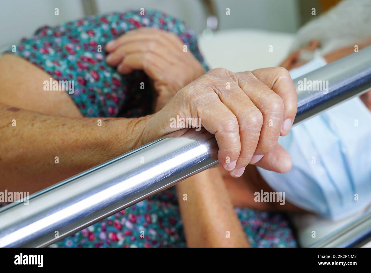 Donna anziana asiatica che tiene la barra del letto mentre si sdraia con speranza in attesa della sua famiglia in ospedale. Foto Stock