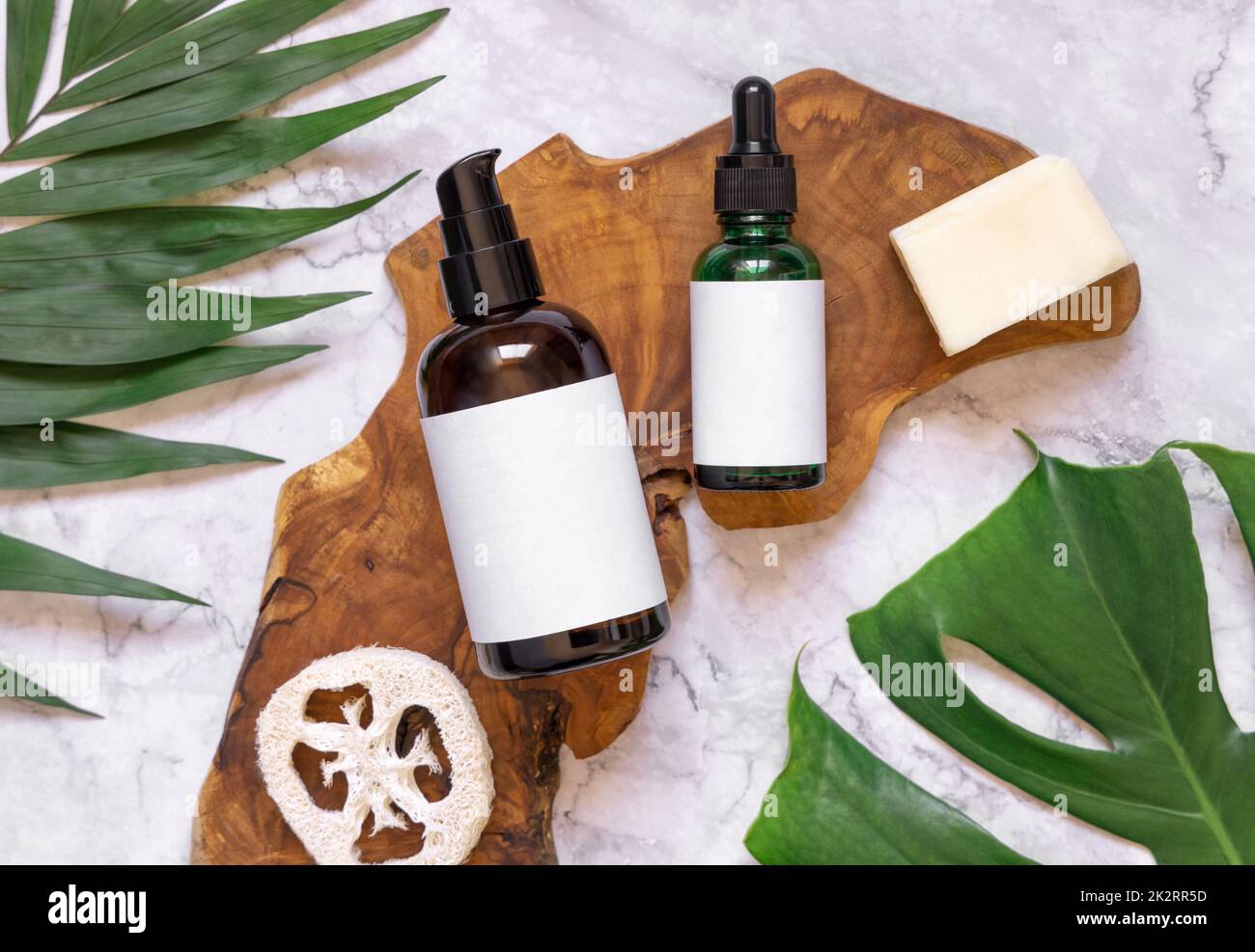 Cosmetici naturali in bottiglie di vetro su un pannello di legno vicino a foglie tropicali, mockup, vista dall'alto Foto Stock