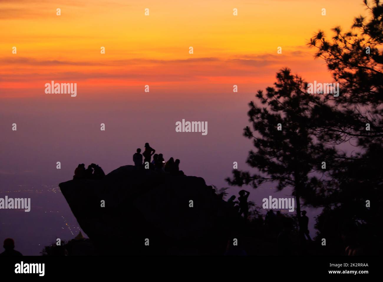 Le silhouette dei viaggiatori si ergono sulle rocce con un'alba chiara. Foto Stock