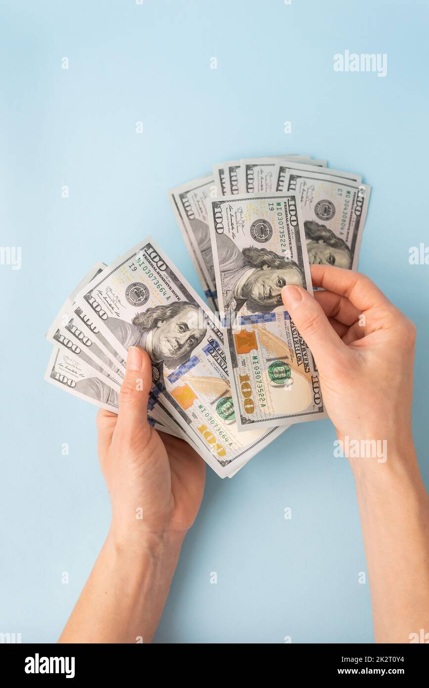 Le mani femminili contano 100 dollari fatture isolate su uno sfondo blu. Foto Stock