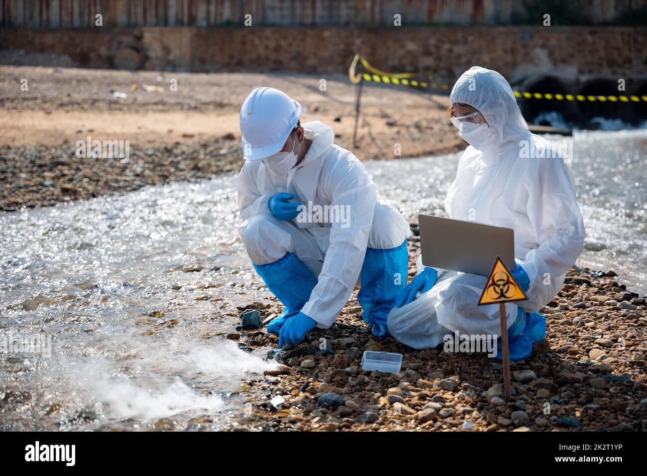 Il biologo indossa tuta protettiva e maschera raccoglie campioni di acque reflue provenienti dall'industria Foto Stock
