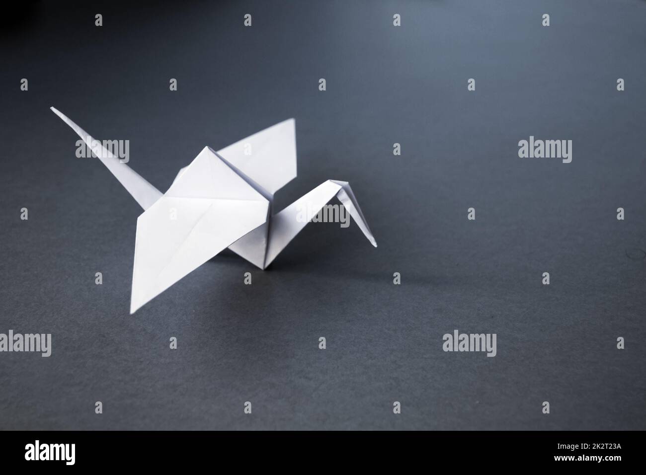 Origami di gru in carta bianca isolato su sfondo grigio Foto Stock