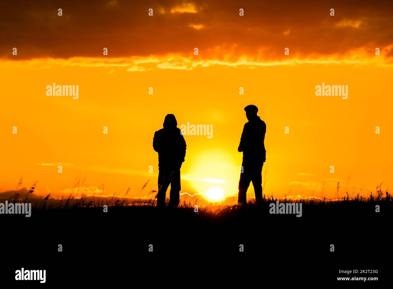 Due silhouette di uomini che parlano al tramonto o all'alba con il cielo e le nuvole drammatici.dialogo e incontro con due persone all'orizzonte e skyline.contorni di persone alla luce del sole.ora d'oro con gli amici Foto Stock