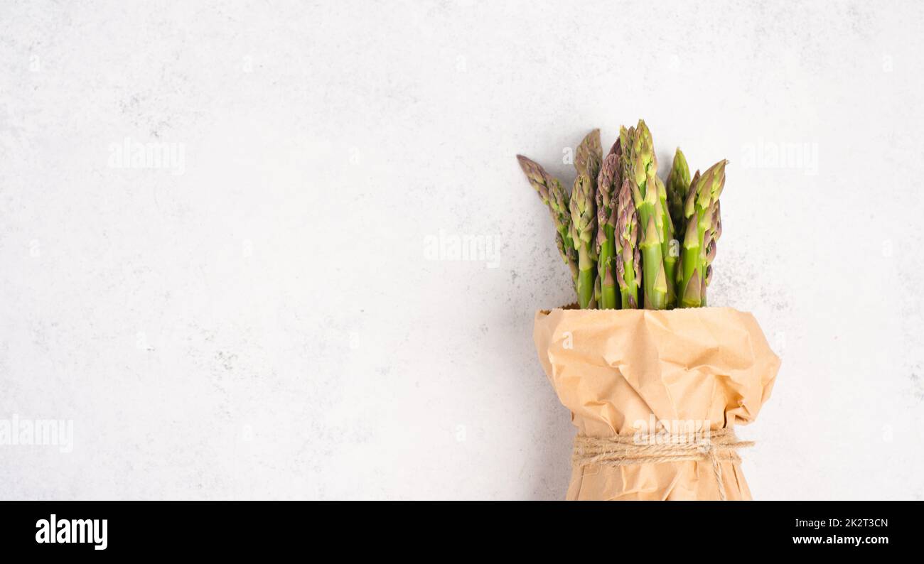 Pacco verde di asparagi freschi su un tavolo bianco testurizzato, verdure in primavera, cibo gourmet cucina, la cottura di un pasto vegano Foto Stock