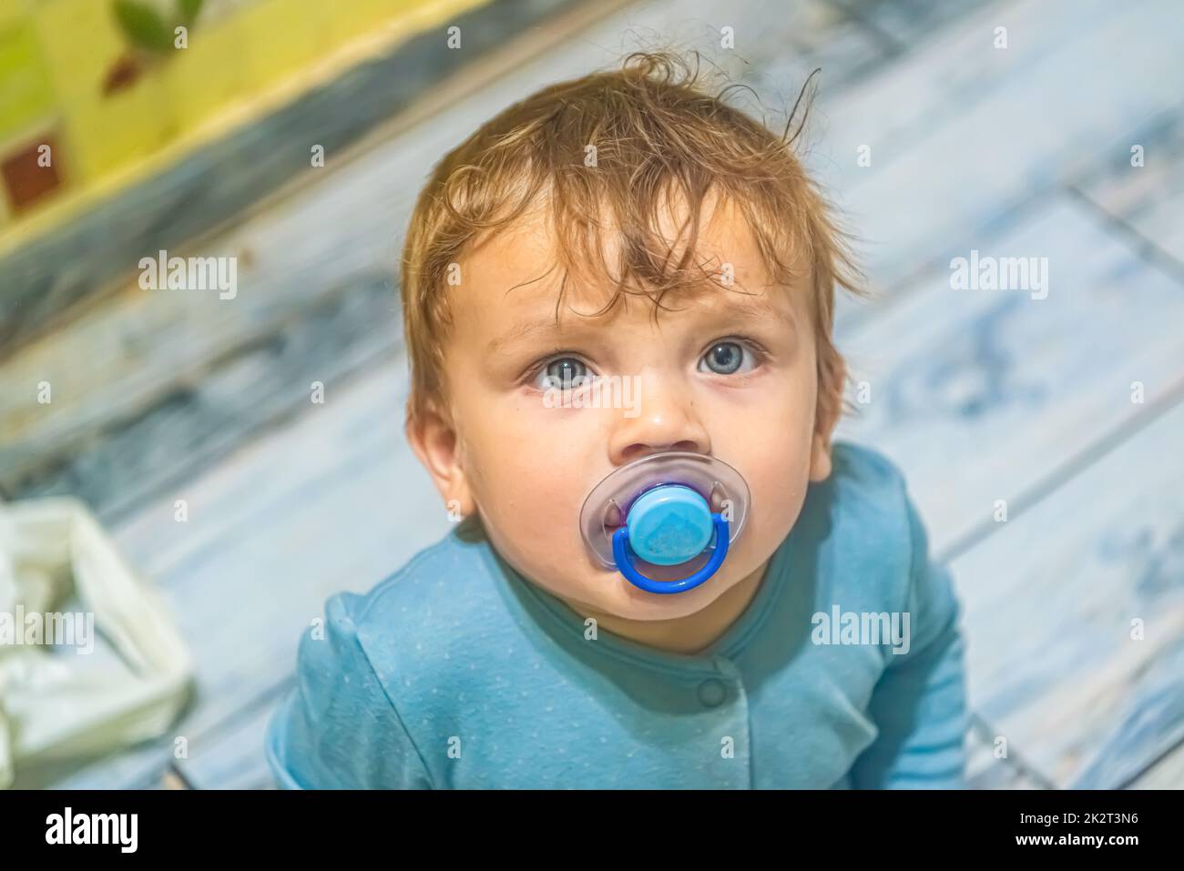 il bambino bianco con gli occhi blu con un succhietto in bocca guarda verso l'alto Foto Stock