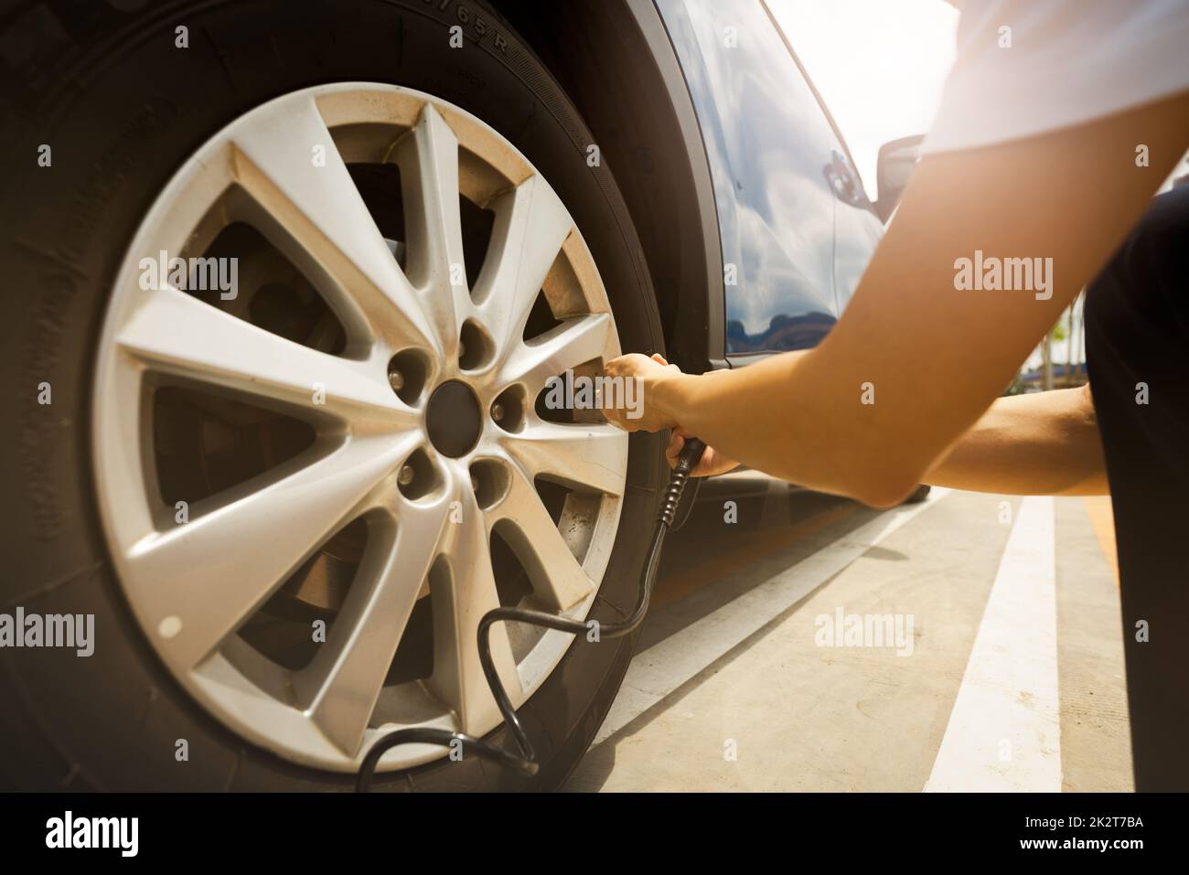 Donna gonfia il pneumatico. Donna che controlla la pressione degli pneumatici e che pompa aria nello pneumatico della ruota dell'automobile. Servizio di manutenzione dell'auto per la sicurezza prima del viaggio. Punto di gonfiaggio pneumatico. Riempimento di aria nello pneumatico dell'auto Foto Stock