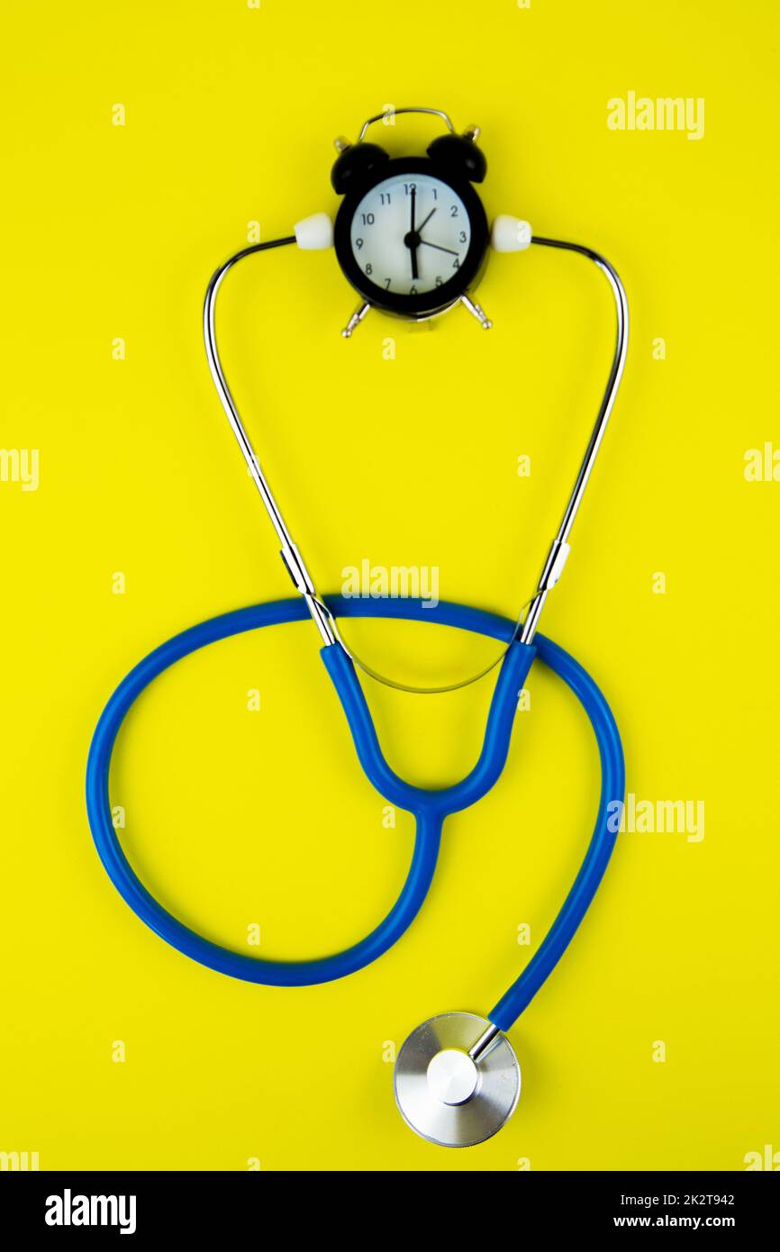 Un orologio di allarme nero con un quadrante bianco si trova su uno sfondo giallo brillante, un fonendoscopio Foto Stock Un orologio di allarme nero con un quadrante bianco si trova su uno sfondo giallo brillante, un fonendoscopio Foto Stock