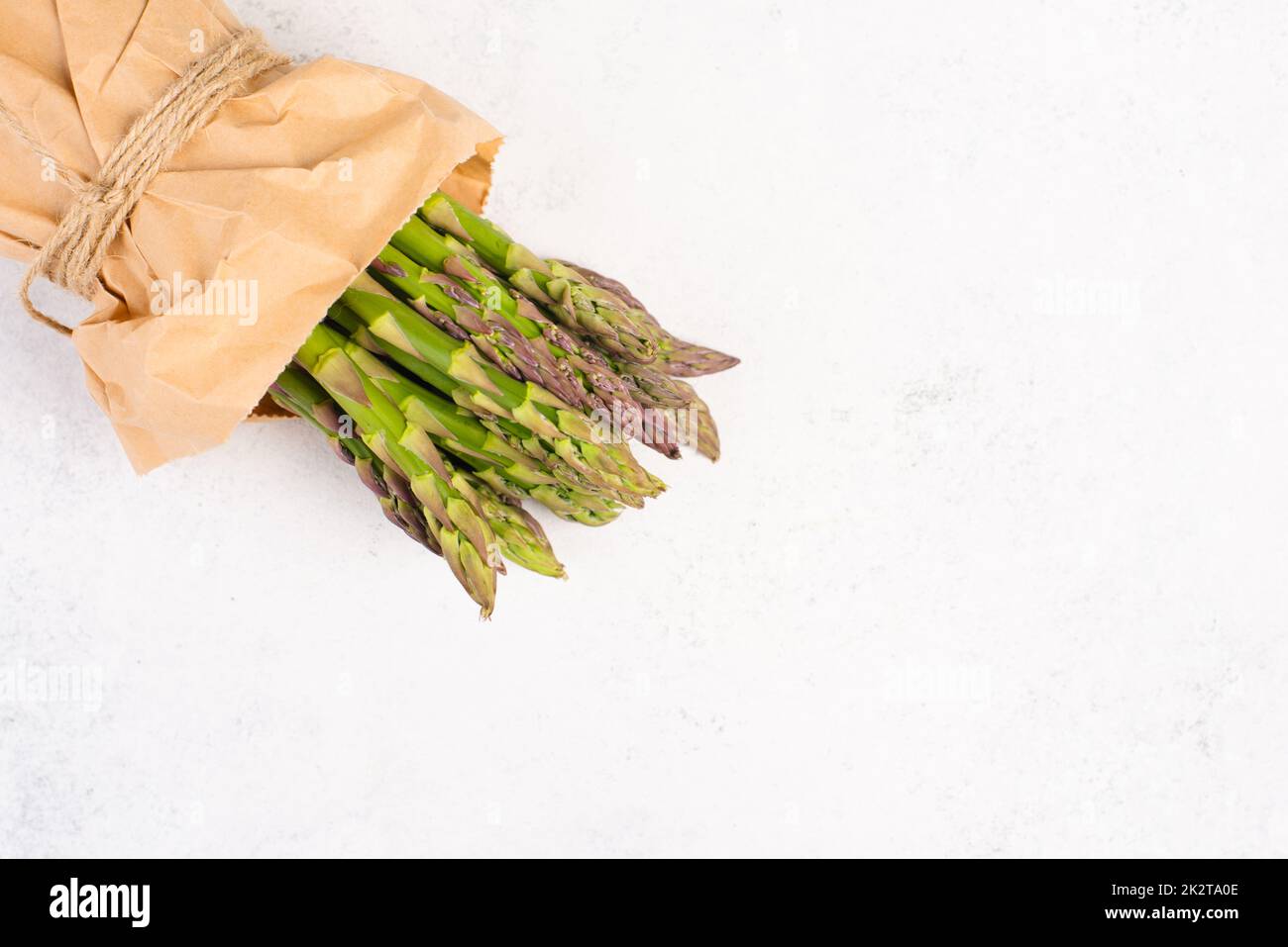 Pacco verde di asparagi freschi su un tavolo bianco testurizzato, verdure in primavera, cibo gourmet cucina, la cottura di un pasto vegano Foto Stock