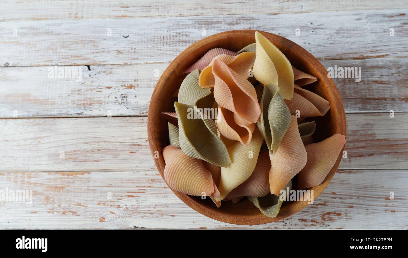 Conchiglie, o 'campane' o 'campane' colorate in un bagno di legno. Un tipo di pasta italiana Foto Stock