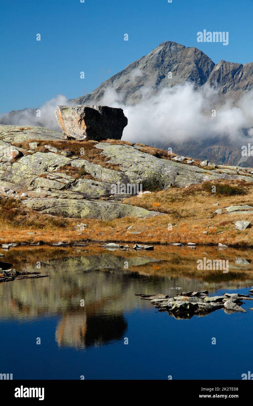 Cime di montagna e grande pietra vicino al bellissimo lago di montagna nelle alpi italiane Foto Stock