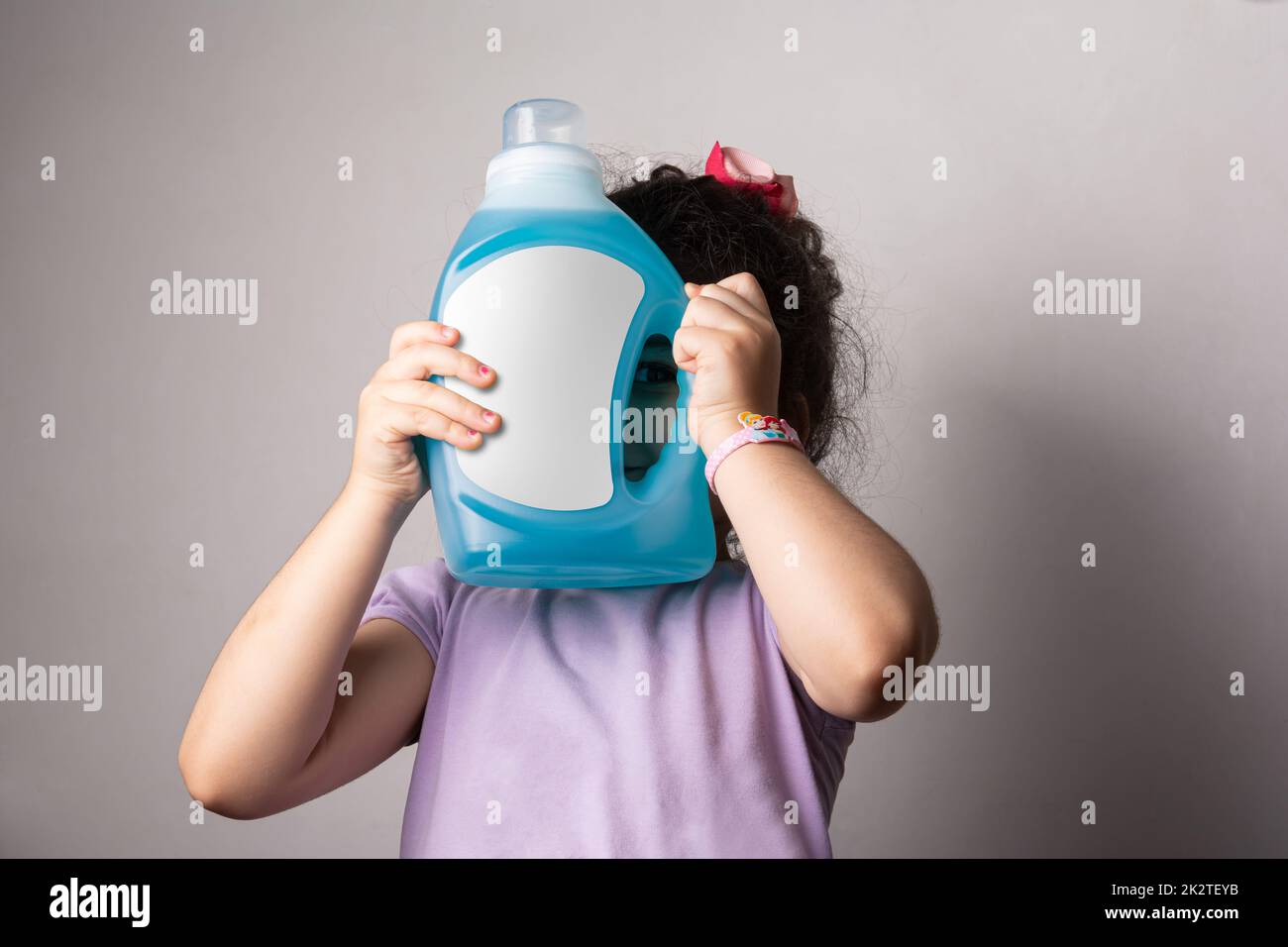 Bambina che tiene una bottiglia di detergente liquido in tessuto davanti alla sua serie di mock-up viso Foto Stock