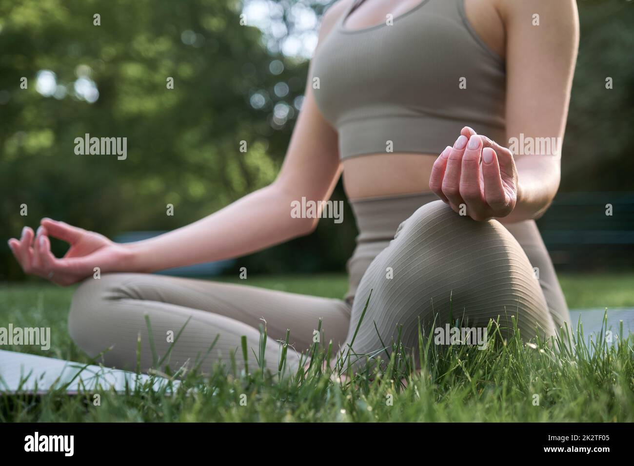 Giovane donna in loto posa seduta su erba verde. Concetto di calma e meditazione Foto Stock