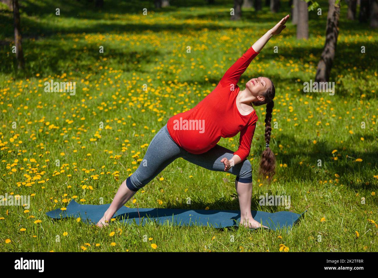 Donna incinta facendo asana Utthita parsvakonasana all'aperto Foto Stock