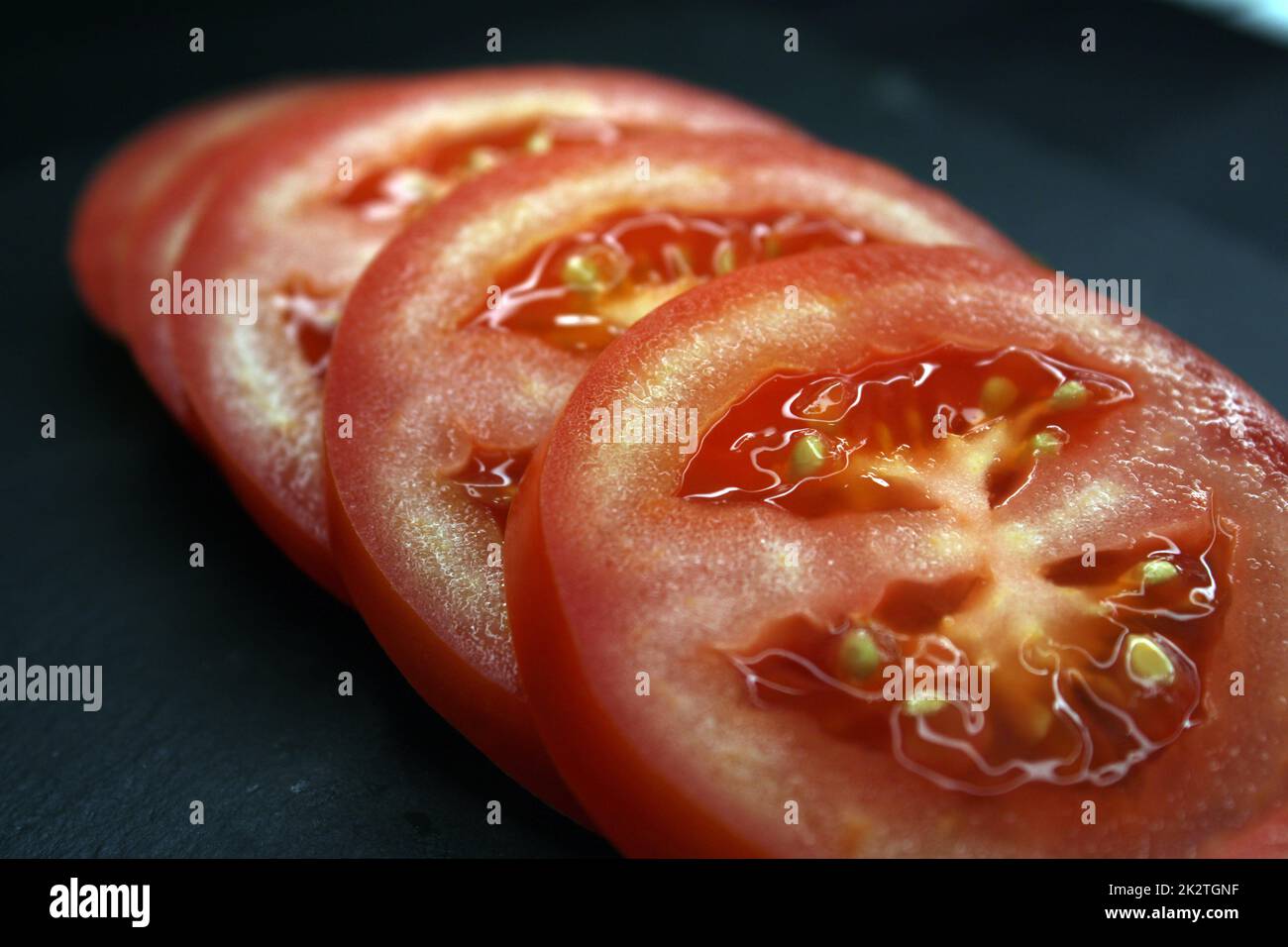 Fette di pomodoro su sfondo nero primo piano. Il concetto di alimentazione sana. Foto Stock