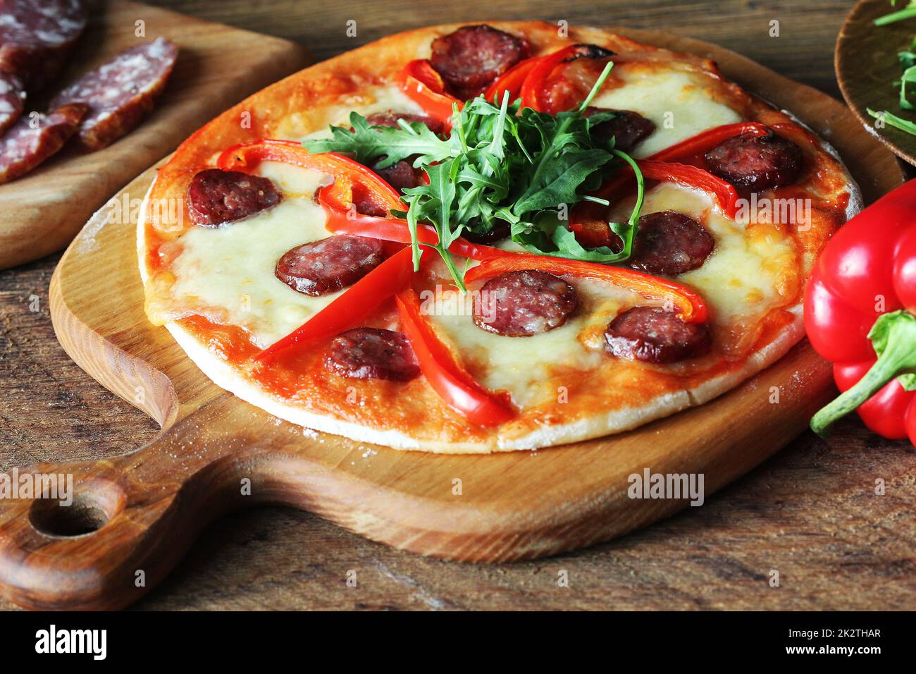 Calda pizza fatta in casa con salsiccia per pizza, paprica, rucola sul tavolo di legno Foto Stock
