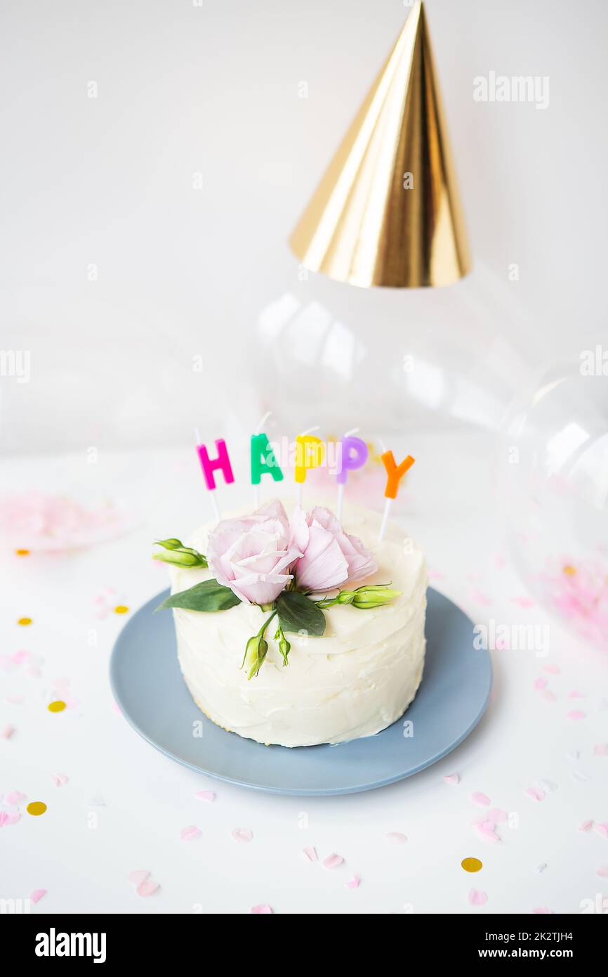 Una bellissima torta bianca, decorata con fiori freschi di eustoma sullo sfondo di dolci e l'iscrizione buon compleanno, palloncini, cappelli. Concetto di vacanza. Foto Stock