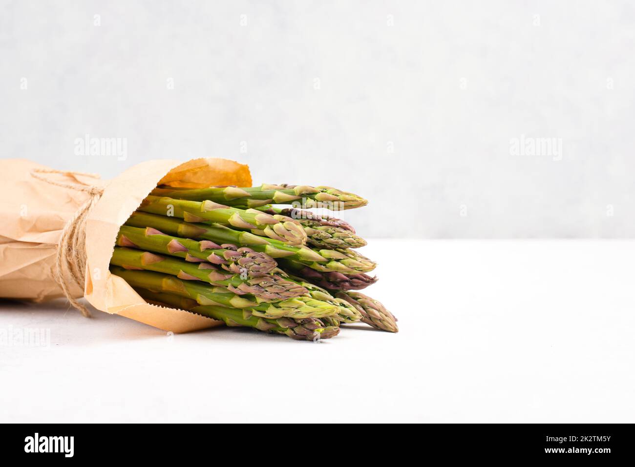 Pacco verde di asparagi freschi su un tavolo bianco testurizzato, verdure in primavera, cibo gourmet cucina, la cottura di un pasto vegano Foto Stock