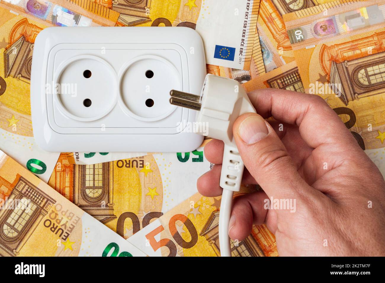 La mano maschio inserisce la spina nella presa elettrica sopra il fondo di soldi Foto Stock