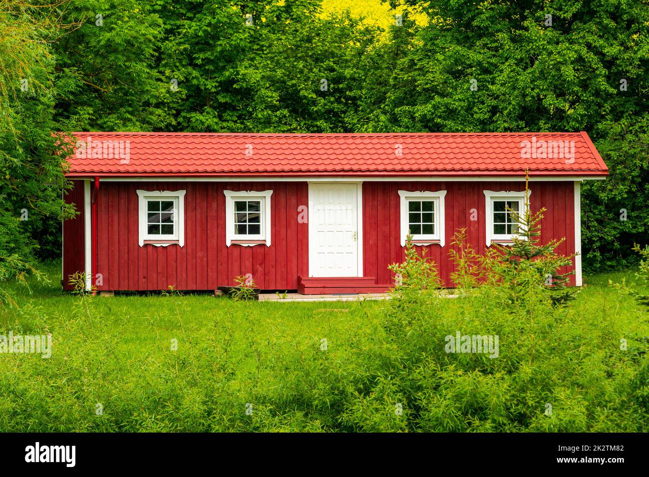 Casa di legno rosso in una natura con un sacco di alberi verdi e prato Foto Stock