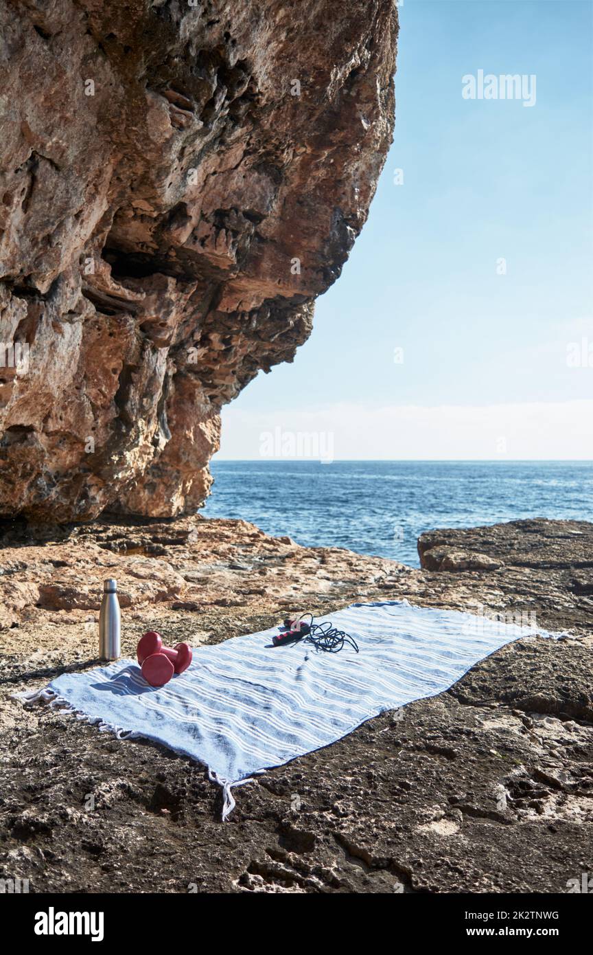 Background di concetto di fitness e sport. Preparazione. Asciugamano, corda da salto, manubri e bottiglia d'acqua, al mare in una giornata d'inverno soleggiata, con un bel cielo blu Foto Stock