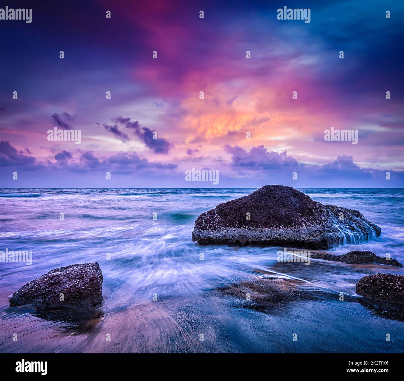 Le onde e le rocce sulla spiaggia di tramonto Foto Stock