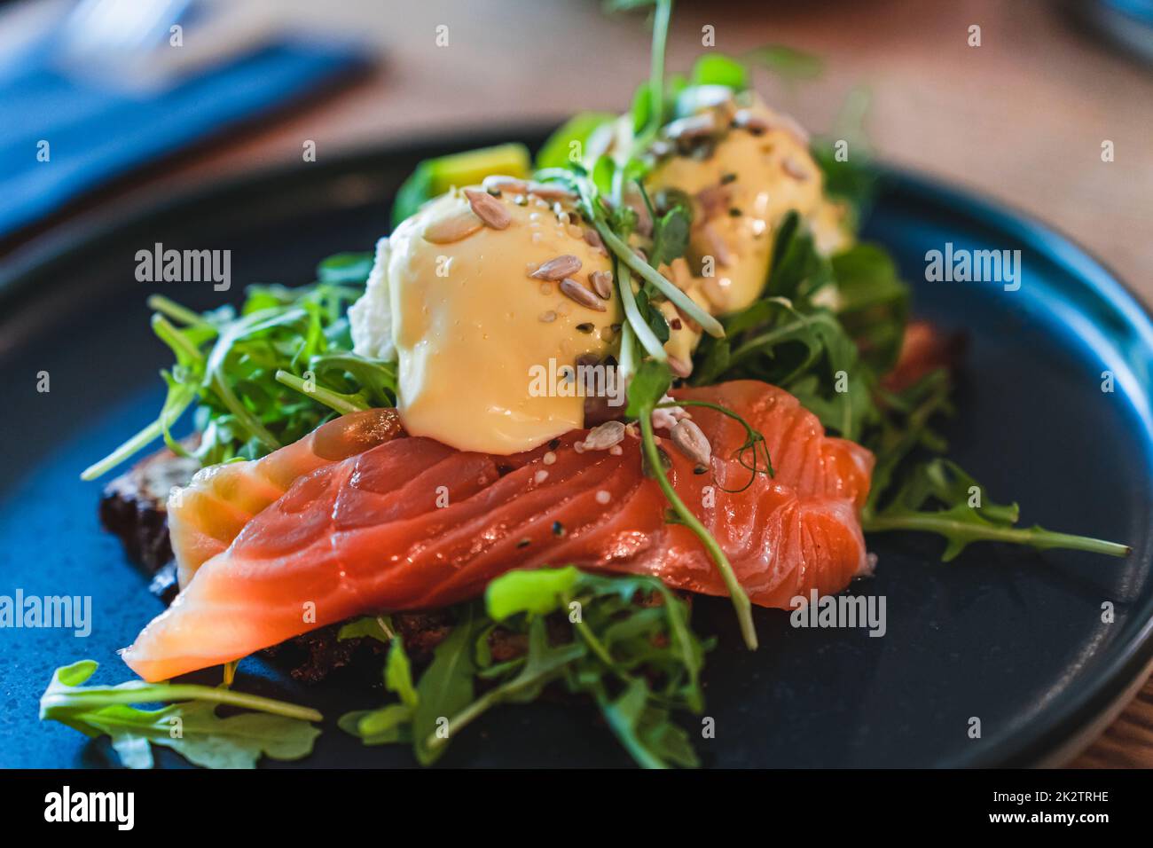 Uova Benedict con salmone e rucola su un piatto nero per la colazione nel ristorante. Messa a fuoco selettiva. Foto Stock