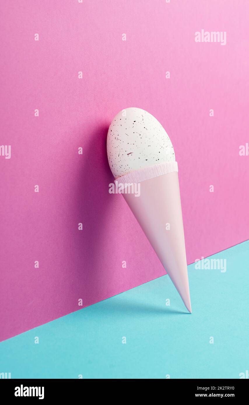 Cono gelato con uovo, sfondo rosa e blu, spazio copia, vacanze di pasqua, stagione estiva, minimalismo e concetto creativo, biglietto di auguri Foto Stock