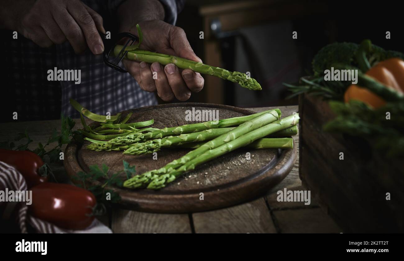 Crop anonimo uomo che sbuccia gli asparagi durante la preparazione sana insalata Foto Stock