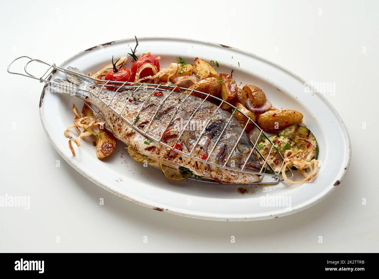 Pesce alla griglia e verdure con patate poste su piatto bianco Foto Stock