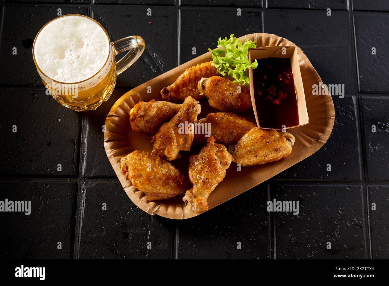 Deliziose ali di pollo e bicchiere di birra messi sul tavolo Foto Stock