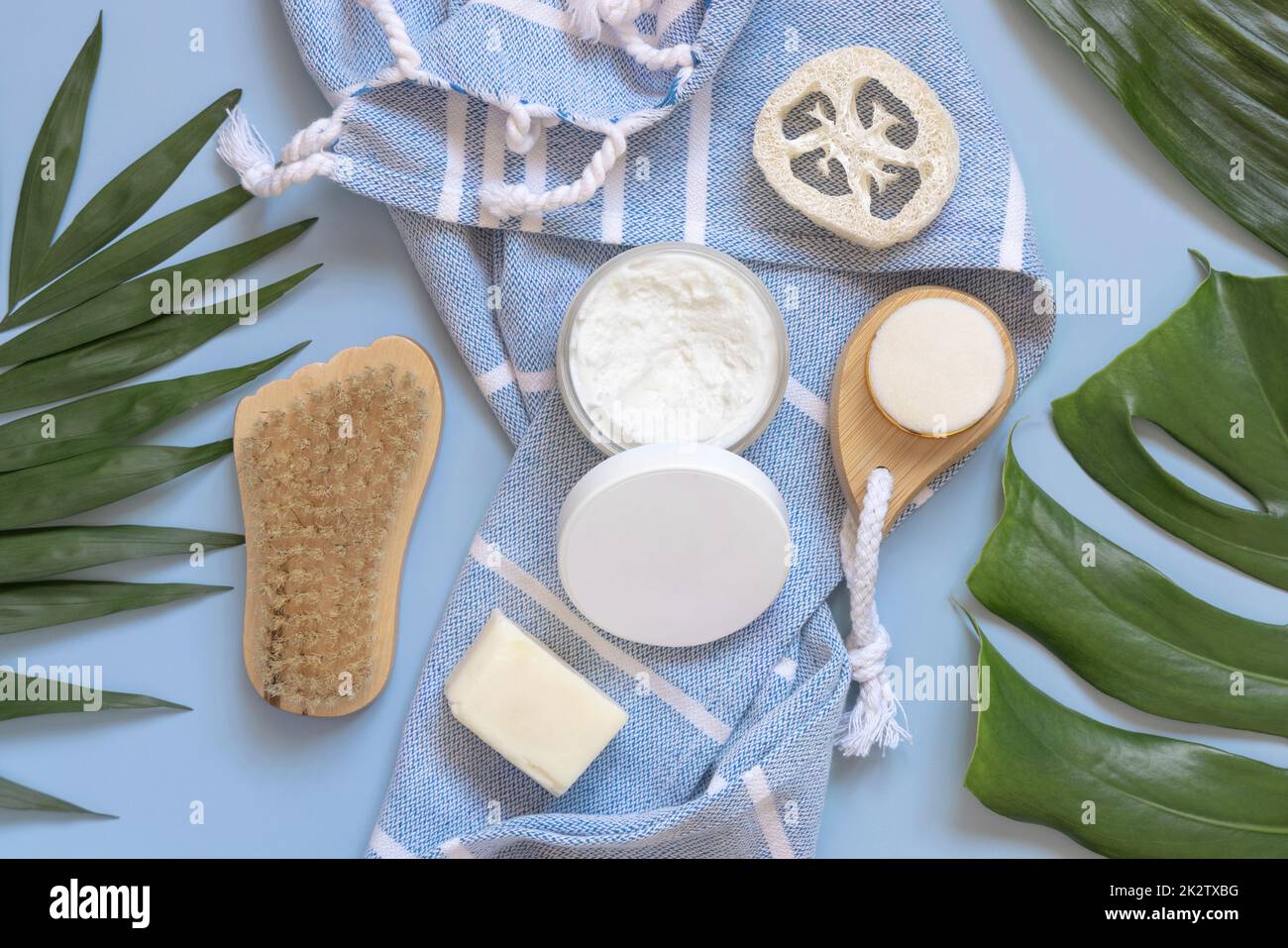 Barra di burro corpo fatta a mano su asciugamano blu vicino alle foglie tropicali vista dall'alto, mockup Foto Stock