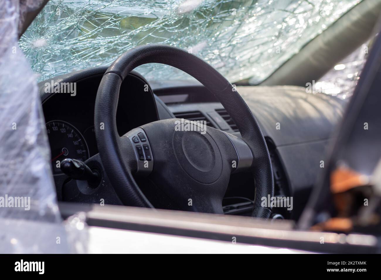 Il volante di una vettura dopo un incidente. Gli airbag lato conducente non si sono attivati. Vista dalla finestra laterale sinistra. Parabrezza rotto con volante. Cruscotto e volante neri polverosi. Foto Stock