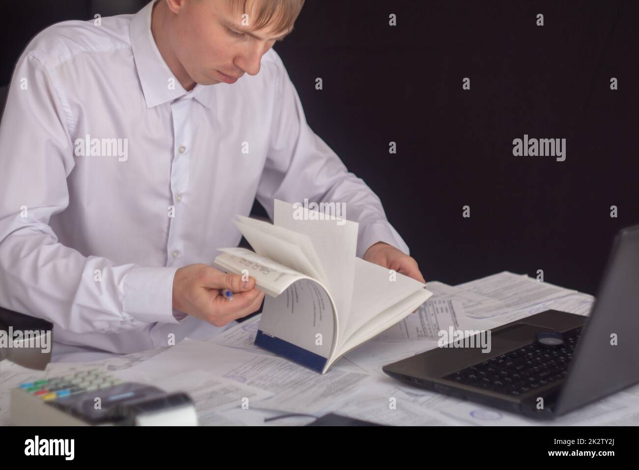 Un uomo d'affari lavora con azioni, obbligazioni, obbligazioni, titoli e documenti in un ufficio notturno. Adempimento degli obblighi di lavorare con documenti in ufficio. Dipendente di un computer portatile in ufficio. Foto Stock