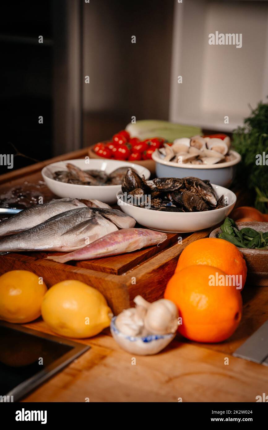 Orata di mare, aglio, gamberi e conchiglie sulla tavola accanto a verdure e frutta. Ingredienti per preparare una deliziosa zuppa. Cucina raffinata. Foto Stock