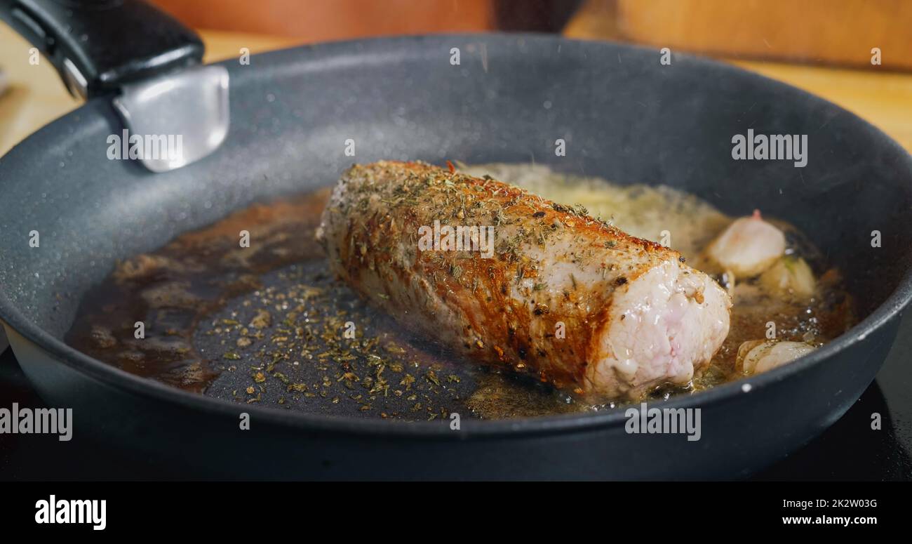 Condimento con erbe in caduta su carne fresca di maiale fritto. Cucina professionale. Immagini spettacolari dalla cucina. Foto Stock
