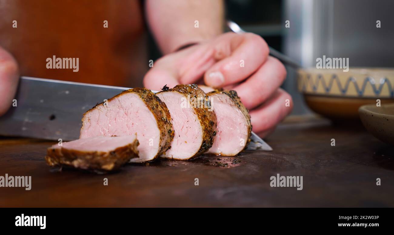 Lo chef taglia la bistecca di maiale piccante sul tagliere rustico su sfondo di legno. Foto Stock