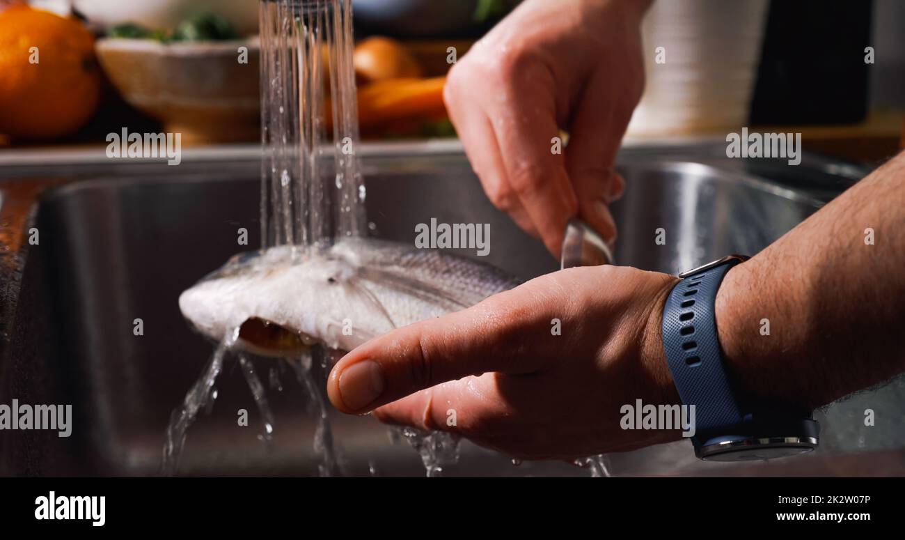 Pulizia del pesce con getto d'acqua prima della cottura. Pesce d'orata con testa dorata. Foto Stock