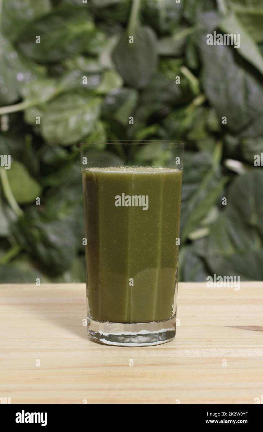 Bicchiere di succo verde fresco con Spinaci sfocati e foglie di lattuga sullo sfondo Foto Stock