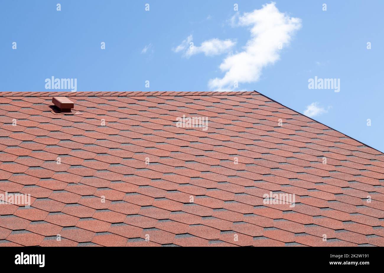 Nuovo tetto con scandole rosse contro il cielo blu. Foto di alta qualità. Tegole sul tetto della casa. Utilizzare per pubblicizzare la fabbricazione e la manutenzione del tetto. Texture macchiata. Copertura conveniente. Foto Stock