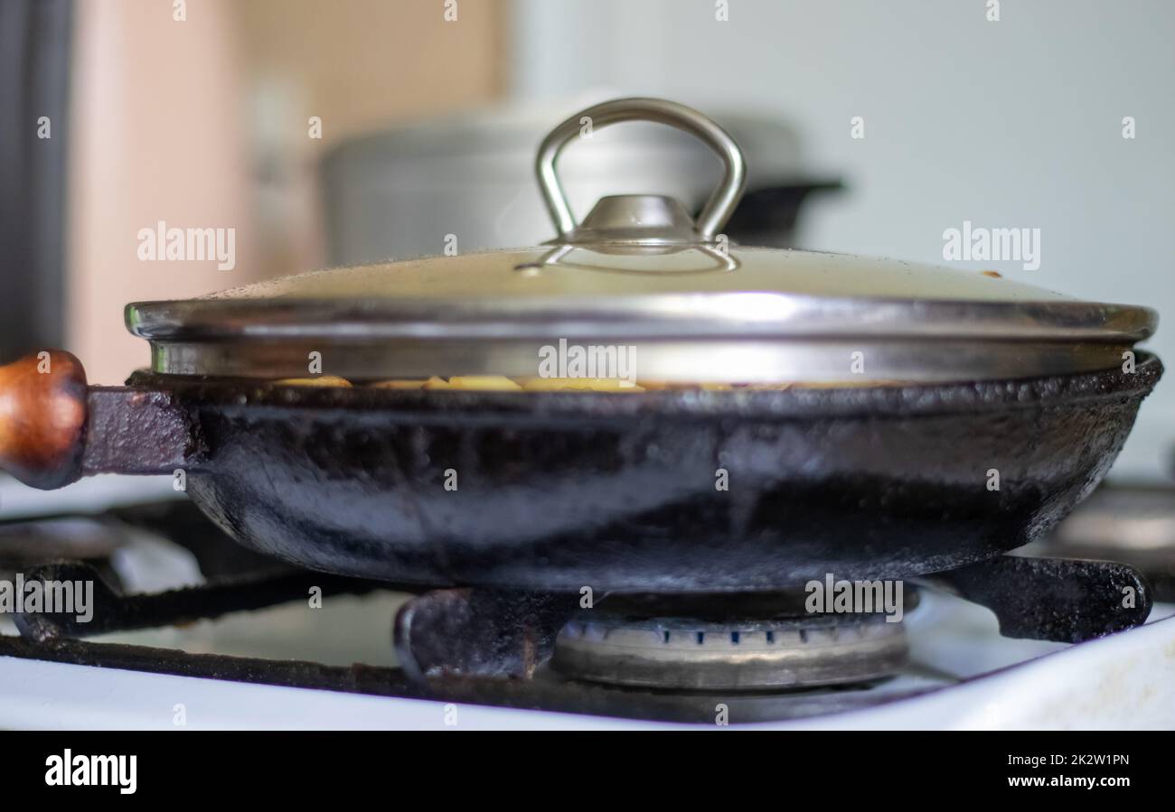 Tostatura di patate fresche in una padella di ghisa con olio di girasole. Una vista su un piano cottura con una padella ripiena di patate fritte dorate in una vera cucina. Cibi cotti in una padella fatta in casa. Foto Stock