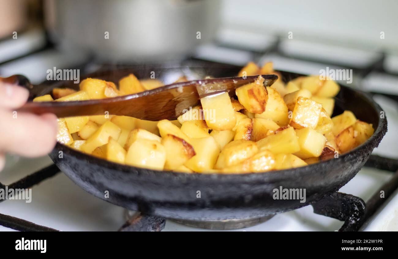 Tostatura di patate fresche in una padella di ghisa con olio di girasole. Una vista su un piano cottura con una padella ripiena di patate fritte dorate in una vera cucina. Cibi cotti in una padella fatta in casa. Foto Stock