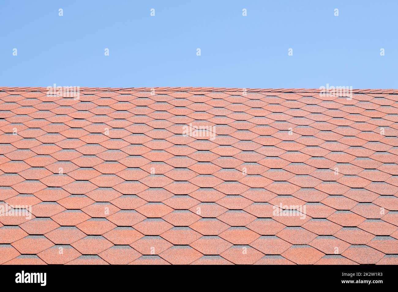 Nuovo tetto con scandole rosse contro il cielo blu. Foto di alta qualità. Tegole sul tetto della casa. Utilizzare per pubblicizzare la fabbricazione e la manutenzione del tetto. Texture macchiata. Copertura conveniente. Foto Stock