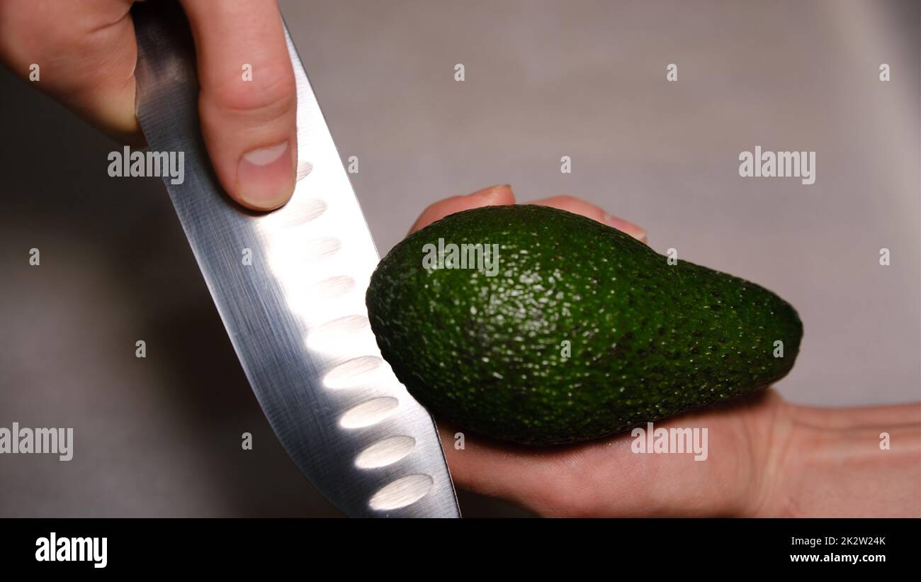 le mani maschili tagliano l'avocado a metà. Avocado fresco maturo, colazione sana, cibo vegetariano Foto Stock