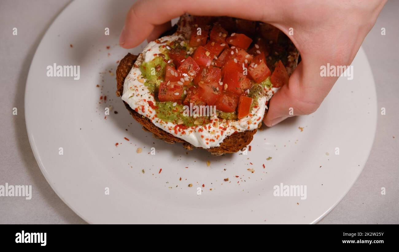 Mano da uomo che taspa i sandwich di avocado, metà di avocado, con arachidi e semi di zucca, tomatos su sfondo bianco Foto Stock