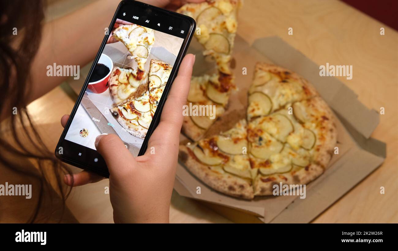 donna mano con smartphone fotografando la pizza al ristorante caffetteria. Pizza vegetariana, cibo vegetariano Foto Stock