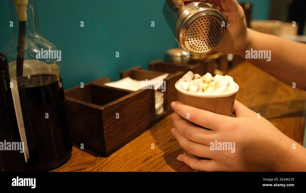 La mano cosparge spezie caffè-cappuccino, cannella, cioccolato. Immagine colorata. Concetto stile di vita Fastfood self-service Foto Stock