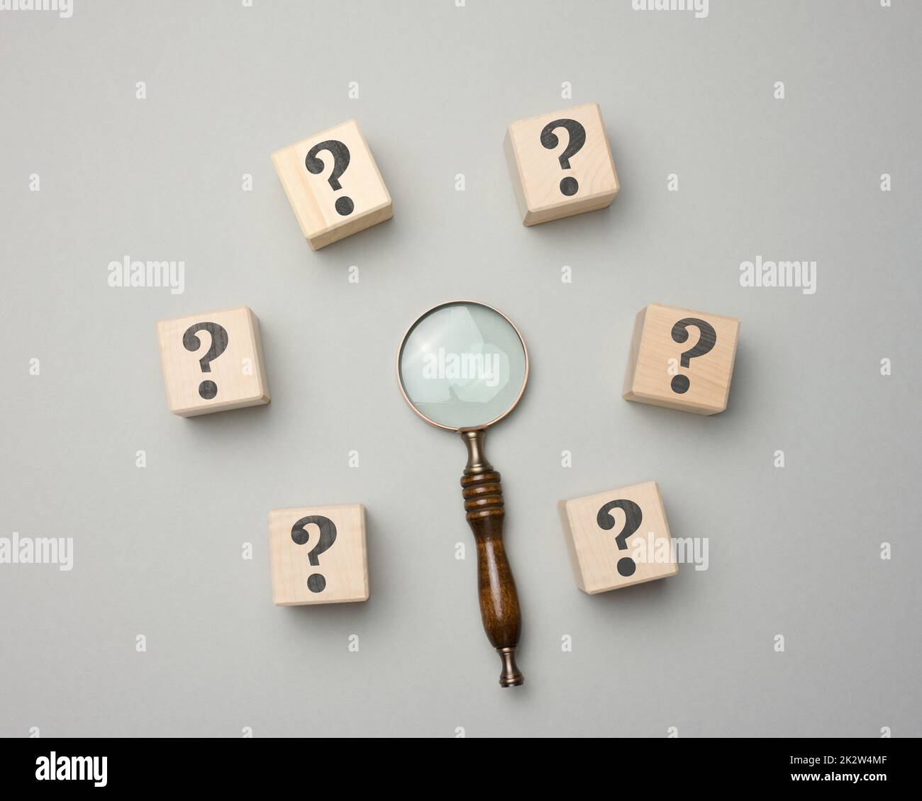 Lente di ingrandimento e cubi in legno con punti interrogativi su sfondo grigio Foto Stock