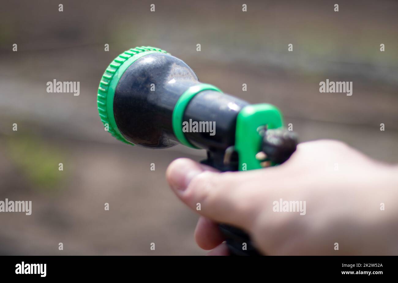 La mano del giardiniere tiene una manichetta con uno spruzzatore e inacqua le piante nel giardino. Atomizzatore verde in mano con una grande lan. Concetto di hobby orticoltura. Innaffiare con un tubo flessibile. Foto Stock