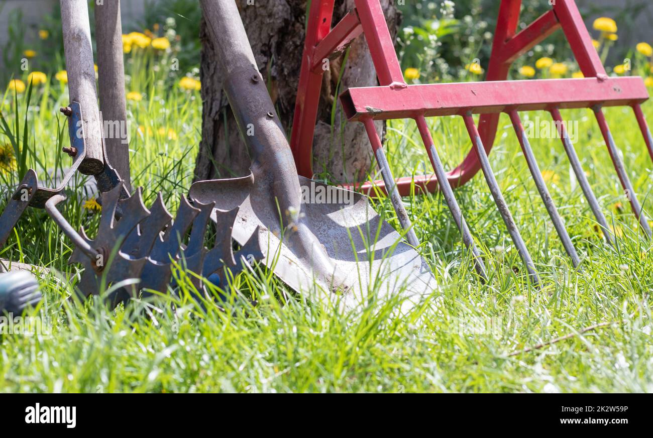 Attrezzi di giardinaggio. Attrezzi da giardino sullo sfondo di un giardino in erba verde. Attrezzatura estiva. Pala, forchetta e lievito in polvere impilati nel giardino all'esterno. Il concetto di attrezzi di giardinaggio. Foto Stock