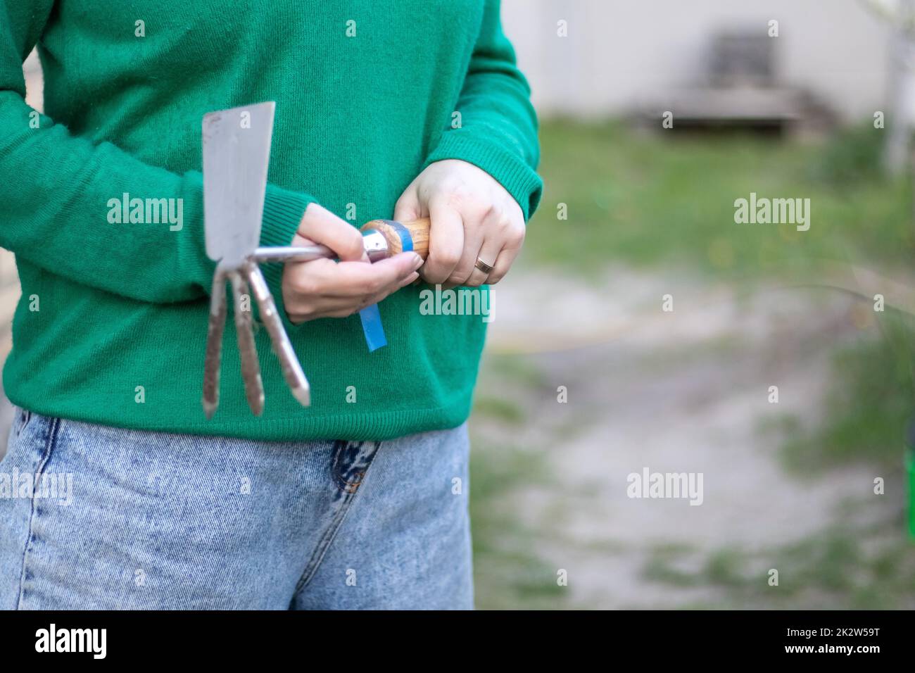 Donna caucasica giardiniere in giardino mostra un rastrello. Il concetto di giardinaggio e l'estate sostenibile. Mano della donna con un attrezzo del giardino. Rastrello del trinciatore per il giardinaggio nelle mani femminili. Posiziona per testo. Foto Stock